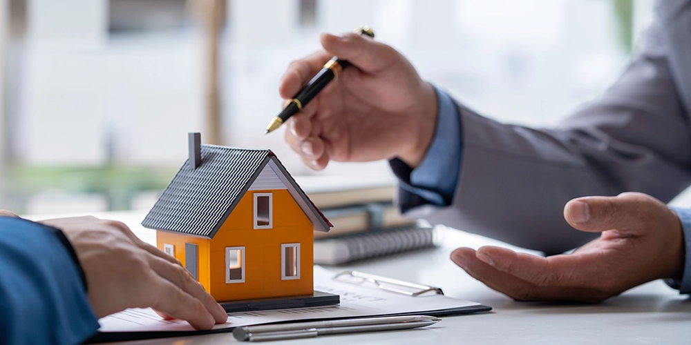 Soluzione legale tra le parti. Contiene le mani delle 2 parti, un contratto, un modellino di casa arancione e 2 penne, sun un tavolo.